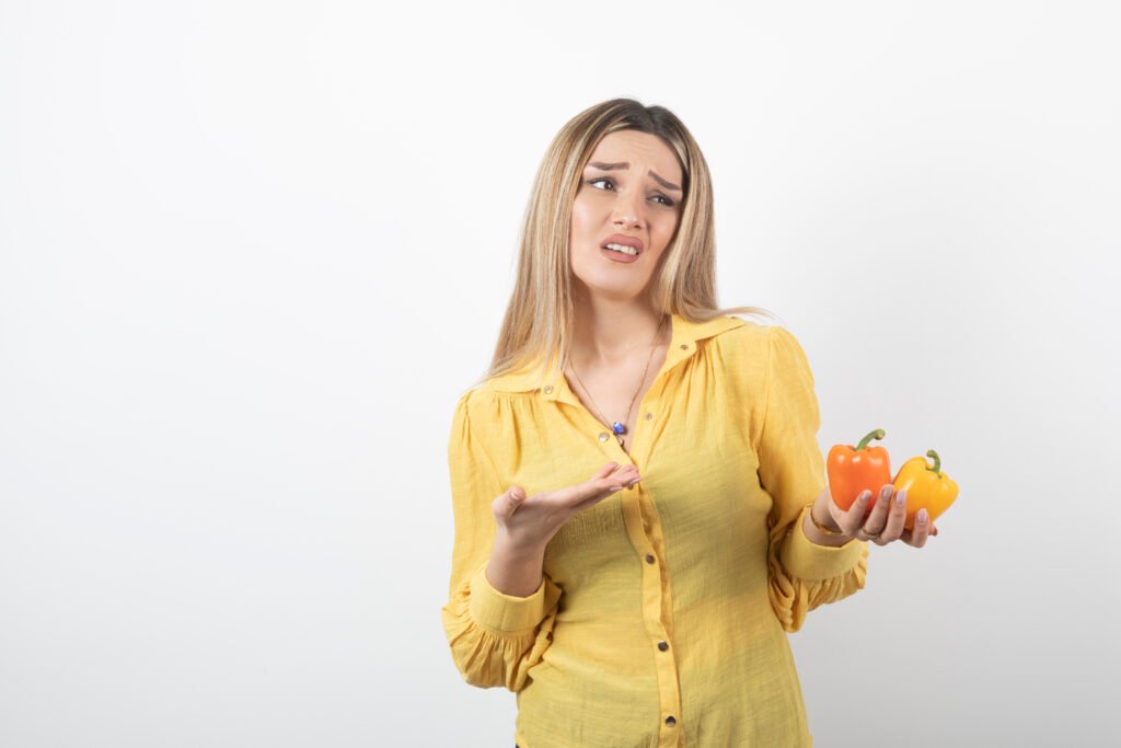 portrait blonde woman holding colorful bell peppers white wall